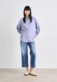 Light blue striped oversized shirt with long sleeves, paired with cropped blue jeans and beige sneakers with a gum sole. Simple design.
