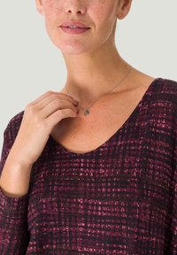 Pitkähihaisen burgundin ja tumman violetin ruutukuosisessa paidassa on avara kaula-aukko. Asusteena on yksinkertainen hopeinen ympyräriipuskaulakoru.