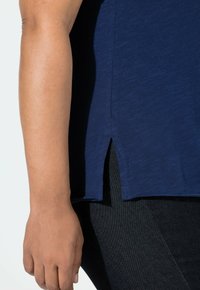 Laivastonsininen lyhythihainen paita, jossa on sivuhalkio, valmistettu pehmeästä, teksturoidusta kankaasta, yhdistetty tummiin, istuviin farkkuihin.