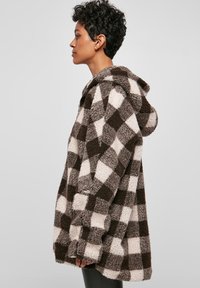 Duks od flisa u smeđoj i krem kariranoj kombinaciji, s opuštenim krojem, velikim džepovima i kapuljačom za toplinu i udobnost.