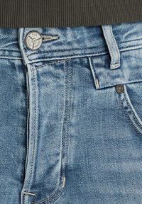 Helle blaue Jeans aus Denim verfügen über einen Metallknopfverschluss, Gürtelschlaufen und kontrastierende Nähte. Sichtbare Textur und leichte Ausbleichungen sind vorhanden.