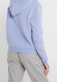 Sudadera color azul claro con capucha ajustable, puños y dobladillo acanalados, combinada con pantalones de chándal grises de tela suave y texturizada.