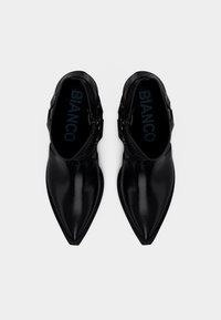 Svarta ankelstövlar med spetsig tå och blank yta, utrustade med justerbara spännen på sidorna och en mjuk innersula.