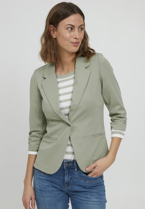 Lichtgroene blazer met een getailleerd ontwerp en één knoopsluiting, met twee voorzakken en opgerolde mouwen over een gestreept top.