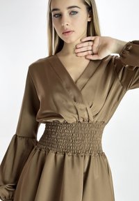 Braunes Satin-Kleid mit tiefem V-Ausschnitt, Puffärmeln und geraffter Taille. Glatte Textur und weicher Fall betonen die fließende Silhouette.