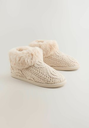 Beige stickade tofflor med en mjuk fuskpälskant, texturerad design och en platt halkfri sula för komfort och stabilitet.