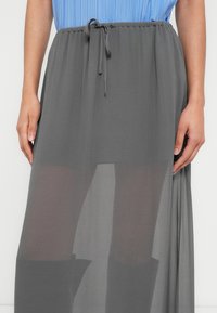 Γκρι, διαφανής φούστα με ελαστική μέση και κορδόνι. Διαθέτει αέρινο σχέδιο και συνδυάζεται με ανοιχτό μπλε τοπ.