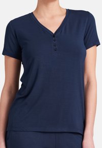 Haut bleu marine à manches courtes avec un col en V et une patte de boutonnage à cinq boutons. Fabriqué en tissu doux, avec une coupe décontractée et une texture subtile.