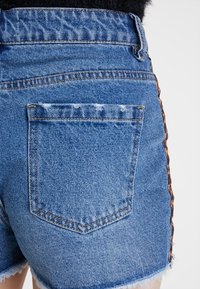 Blå denimshorts med fransad nederkant, med en bakficka och kontrasterande sömmar längs sidan.