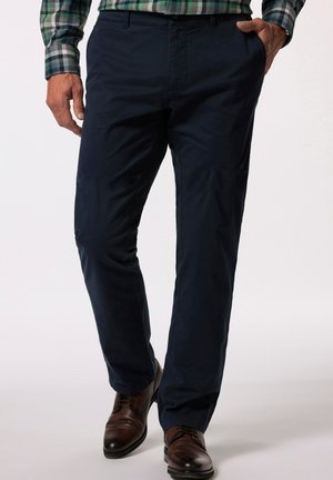 Marineblaue Hose aus glattem Stoff mit geradem Bein und Fronttaschen, kombiniert mit braunen Lederschuhen.