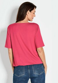 Kurzärmliges, Rundhals-Top aus lebhaft pinkem Stoff mit glatter Textur. Kombiniert mit blauen Jeans mit detaillierten Gesäßtaschen.