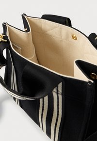 Borsa tote nera in canvas con strisce verticali crema e nere, accessori dorati e interni in tessuto beige trapuntato con molteplici scomparti.