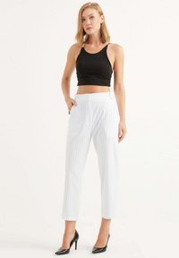 Zwart cropped tanktop gecombineerd met witte pantalons met streepjes en hoge taille. De pantalons hebben een rechte pasvorm en zijzakken. Zwarte hakken.