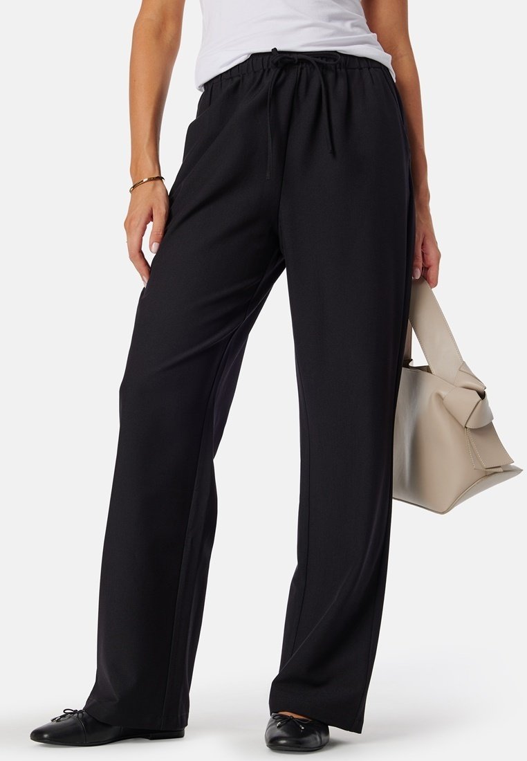 Zwarte, wijde broek met elastische tailleband. Glad materiaal met een relaxte pasvorm. Gecombineerd met een lichte tas en zwarte ballerina's.