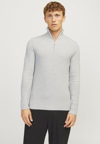 Suéter de canalé gris claro con cuello alto y media cremallera, combinado con pantalones de canalé negros. La tela es suave y texturizada.