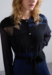 Schwarzes und dunkelblaues Hemdkleid aus einer Mischung von Materialien, darunter durchsichtige und romantische Spitze, mit Knöpfen und einem gebundenen Taillenakzent.