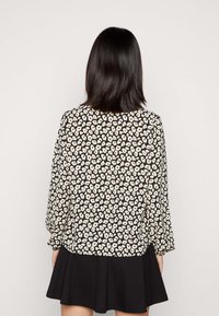 Blusa preta com padrão floral creme, mangas longas e um corte descontraído, combinada com uma saia plissada preta. Textura suave em toda a peça.
