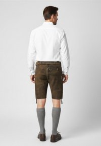 Bruine leren shorts met een trekkoord in de taille, gecombineerd met grijze kniekousen en donkere schoenen. Witte shirt losjes gedragen.
