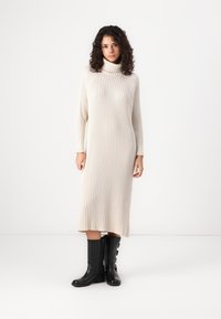 Cream ribbed turtleneck dress, mid-length with long sleeves, paired with black knee-high boots featuring side buttons.