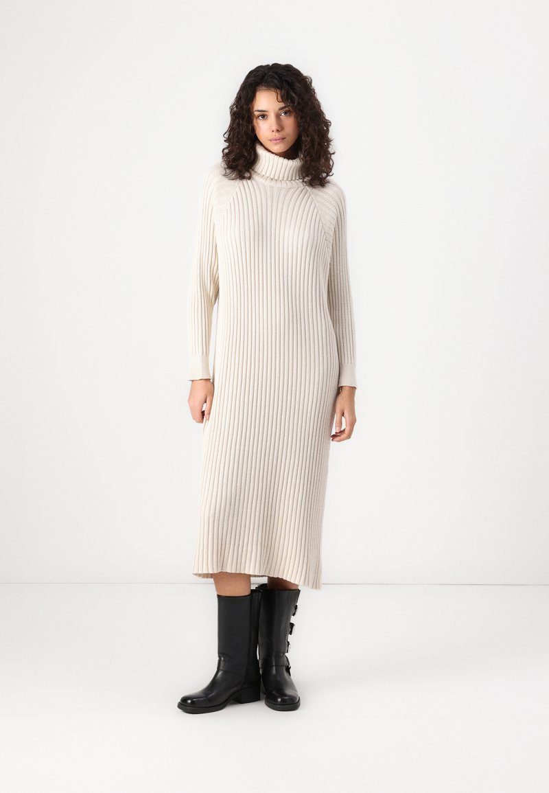 Cream ribbed turtleneck dress, mid-length with long sleeves, paired with black knee-high boots featuring side buttons.