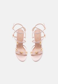 Sandales à talons roses avec plusieurs brides, ornées de légers accents floraux. Matière lisse et brillante, design à bout ouvert.