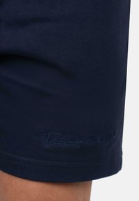 Shorts sportivi blu navy realizzati in tessuto liscio. Presentano un logo ricamato in un colore coordinato sull'orlo inferiore. Design con vestibilità regolare.