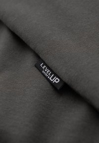 Gros plan sur une étiquette noire avec texte blanc « "LEVEL UP" » cousue sur un tissu sombre et lisse.