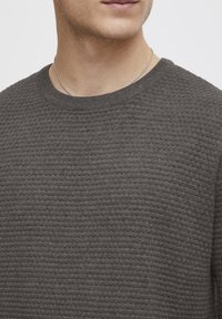 Maglione grigio con un motivo di maglia textured, scollo tondo e finiture a coste sul collo. Vista ravvicinata che mette in evidenza i dettagli del tessuto.