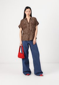 Leopardmönstrad kortärmad skjorta i brunt och beige, i kombination med blå vida jeans och en röd handväska, kompletterad av spetsiga röda skor.