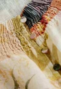 Gros plan sur un tissu avec des détails froncés multicolores et de petits boutons recouverts du même tissu, sur un fond texturé clair.