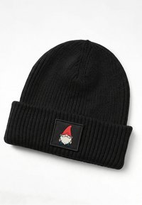 Black knitted beanie with a ribbed texture and fold-over cuff. Features a square patch depicting a cartoon gnome with a red hat and white beard.