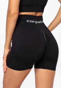 Black athletic shorts with a high waistband. Features textured ribbing and gathers at the back for enhanced fit. Logo displayed on the waistband.