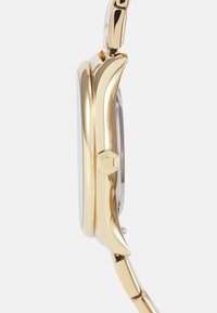 Gold-tone watch with a sleek, curved case, hexagonal crown, and polished finish. The strap features elongated links for a refined look.