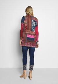 Mönstrad lång kofta i flera färger med långa ärmar. Har blommiga och geometriska designmönster i röd, blå och jordnära toner. Matchas med broderade jeans.