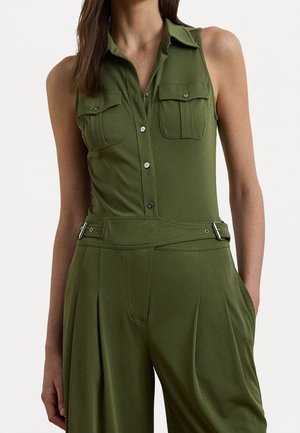Ärmelloser olivgrüner Jumpsuit mit Knopfleiste vorne, zwei Brusttaschen, tailliertem Gürtel und weit geschnittenen Hosen, getragen von einer Frau.