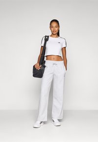 T-shirt branco cropped com riscas pretas, calças de moletom cinzentas com uma cintura elástica e uma pequena bolsa preta cruzada, combinadas com sapatilhas brancas.