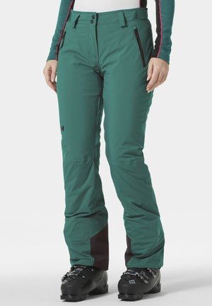 Grüne Skihosen aus strapazierfähigem Material mit einem schlanken Design, Reißverschlusstaschen und kontrastierenden dunklen Akzenten am Knöchel.