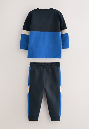 Sinine ja mereväe puuvillane dressikomplekt, mis sisaldab toonitud pikkade varrukatega pluusi ning kitsanevaid pükse, mille külgedel kontrastsed detailid.