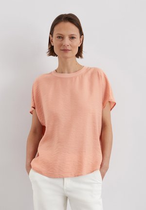 T-shirt à manches courtes de couleur pêche avec une coupe décontractée et un col en rib, présentant un tissu texturé et un design à ourlet arrondi.
