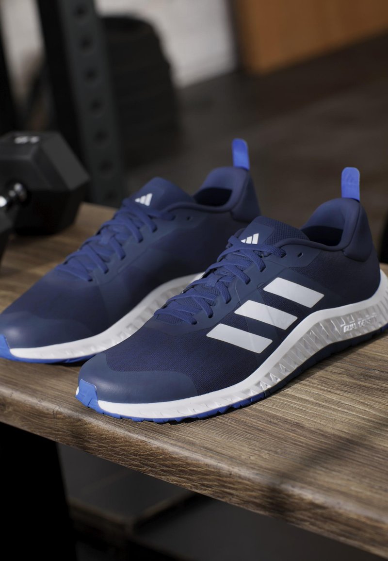 Navy athletic shoes with a textured upper, white three-stripe logo, and a white sole featuring a serrated pattern. Blue accent on the heel.