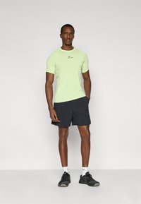 Κοντομάνικο, ανοιχτοπράσινο μπλουζάκι Nike Pro με μαύρο λογότυπο, συνδυασμένο με μαύρο σορτς και μαύρα αθλητικά παπούτσια. Απλός σχεδιασμός, εφαρμοστή γραμμή.