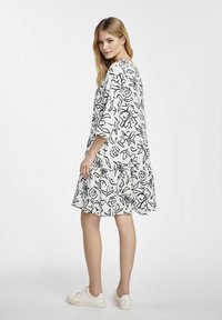 Czarny kwiatowy wzór na białej sukience do kolan z rękawami o długości trzy czwarte, luźnym kroju i rozkloszowanym dolnym wykończeniem, w zestawieniu z białymi sneakersami.