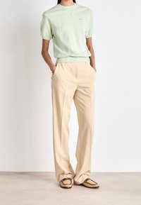 Light green short-sleeve sweater, beige tailored pants with side pockets, and brown woven loafers with accents. Simple, modern design.