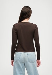 Haut à manches longues côtelé marron avec un décolleté large, associé à un jean taille haute bleu clair avec des poches arrière. Texture de tissu lisse.