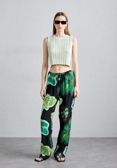 Top corto acanalado verde claro combinado con pantalones negros que presentan grandes patrones florales en verde y amarillo. La modelo lleva gafas de sol negras y sandalias.