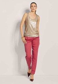 Gouden pailletten tanktop met een ronde hals, gecombineerd met roze op maat gemaakte broeken en bordeauxrode hoge hakken, tegen een neutrale achtergrond.