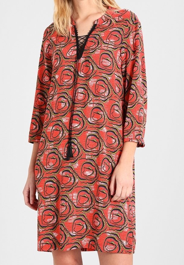 Punainen mekko, jossa on abstrakti pyöreä kuvio; siinä on v-pääntie naruauhalla, kolmanneksen pituiset hihat ja rento istuvuus.