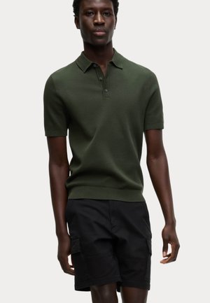 Short-sleeve polo shirt in dark green knitted fabric, featuring a five-button placket and a ribbed hem, paired with black cargo shorts.