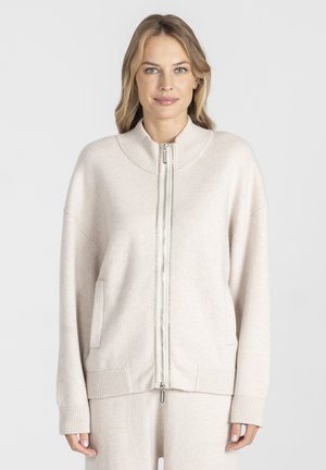 Jasno beżowy sweter na zamek, wykonany z miękkiego materiału, z prążkowanym kołnierzem, mankietami i dołem, a także z dwoma bocznymi kieszeniami.