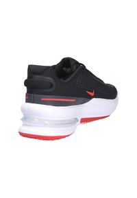 Zapatilla deportiva negra con parte superior perforada, acentos rojos y una entresuela blanca con amortiguación Air visible. Talón texturizado y suela exterior de goma duradera.